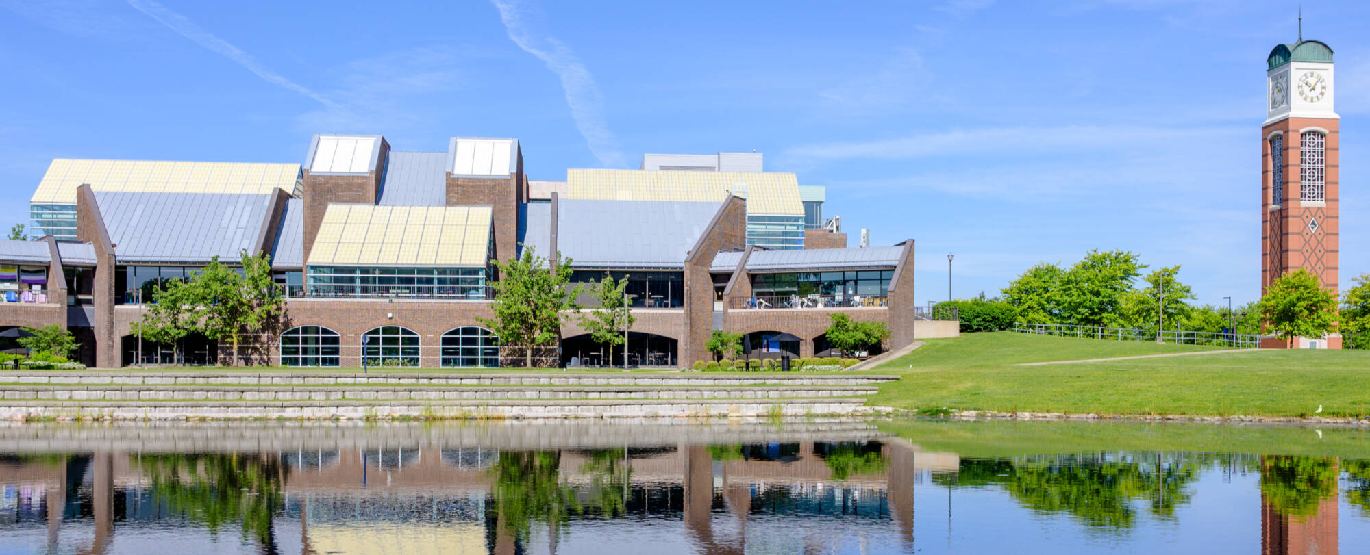 On the warm morning of May 29, the Russel H. Kirkhof Center and the Cook Carillon Tower are reflected on Zumberge Pond.